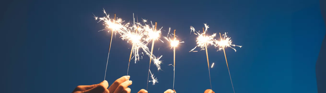 Des mains brandissant des cierges magiques sous un ciel nocturne, symbolisant un nouveau départ et la motivation à tenir ses bonnes résolutions pour l'année à venir