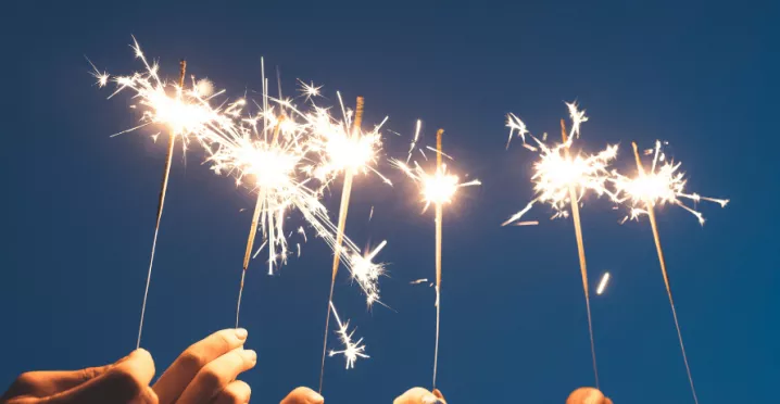 Des mains brandissant des cierges magiques sous un ciel nocturne, symbolisant un nouveau départ et la motivation à tenir ses bonnes résolutions pour l'année à venir