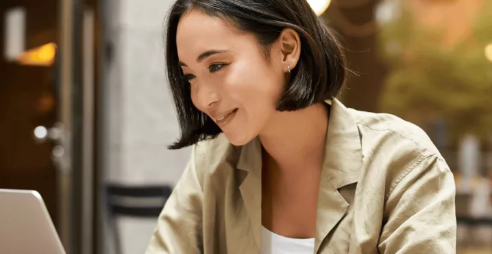 Femme souriante travaillant sur un ordinateur portable en terrasse - Pluxee Luxembourg, solutions pour le bien-être au travail