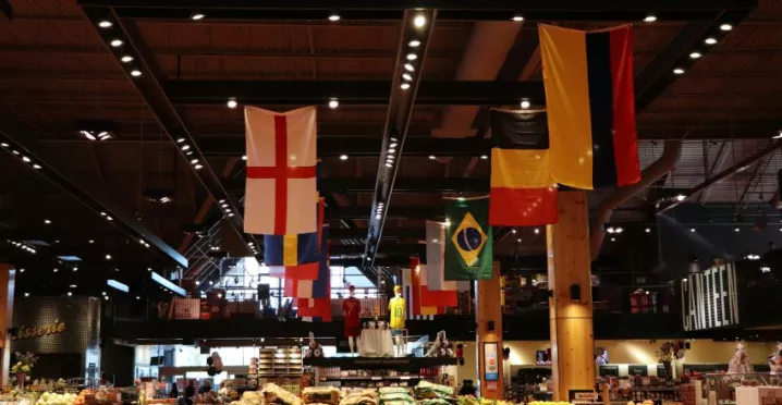 Étal de produits frais dans un marché alimentaire couvert, avec plusieurs drapeaux internationaux suspendus au plafond.