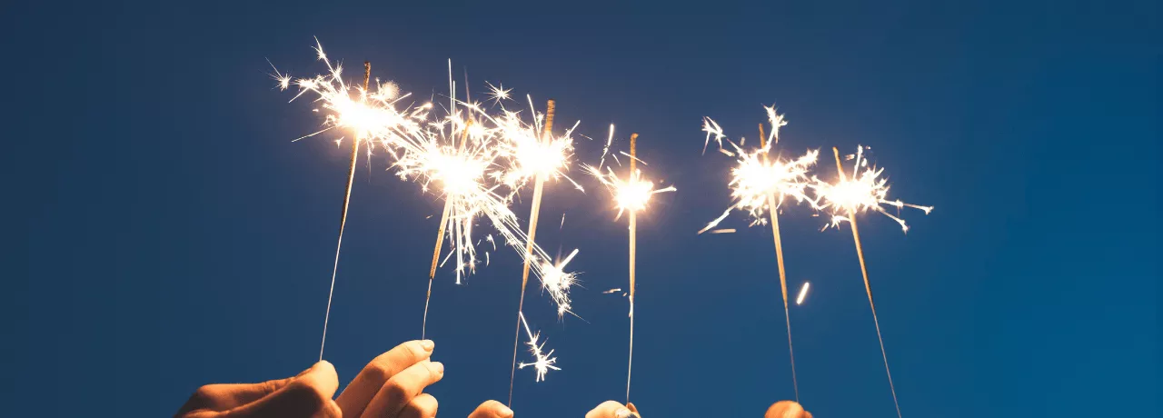 Des mains brandissant des cierges magiques sous un ciel nocturne, symbolisant un nouveau départ et la motivation à tenir ses bonnes résolutions pour l'année à venir