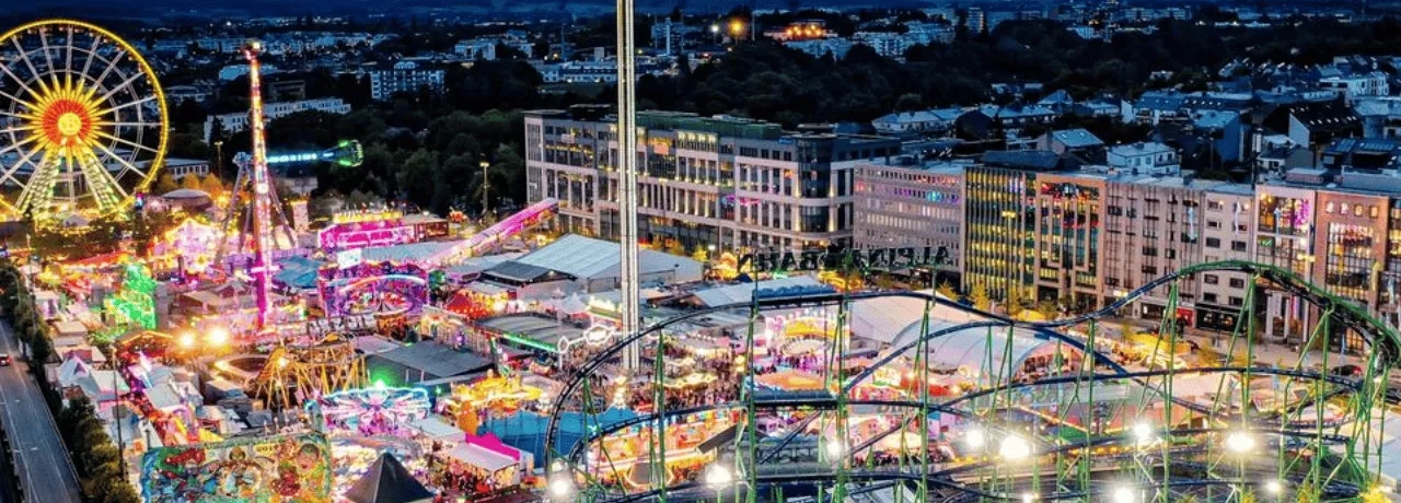 Schueberfouer Luxembourg au coucher du soleil avec grande roue illuminée, manèges et attractions: idée de sortie familiale avant la rentrée scolaire, recommandée par Pluxee Luxembourg.