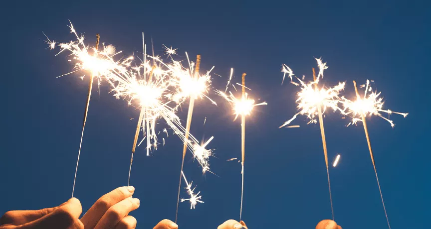 Des mains brandissant des cierges magiques sous un ciel nocturne, symbolisant un nouveau départ et la motivation à tenir ses bonnes résolutions pour l'année à venir