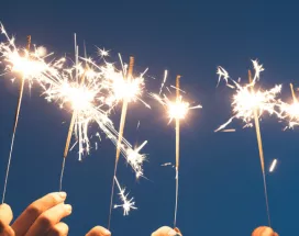 Des mains brandissant des cierges magiques sous un ciel nocturne, symbolisant un nouveau départ et la motivation à tenir ses bonnes résolutions pour l'année à venir