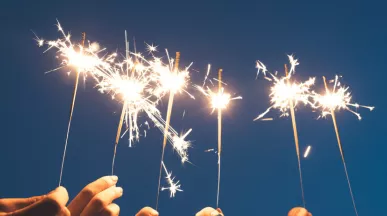 Des mains brandissant des cierges magiques sous un ciel nocturne, symbolisant un nouveau départ et la motivation à tenir ses bonnes résolutions pour l'année à venir