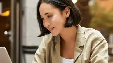 Femme souriante travaillant sur un ordinateur portable en terrasse - Pluxee Luxembourg, solutions pour le bien-être au travail